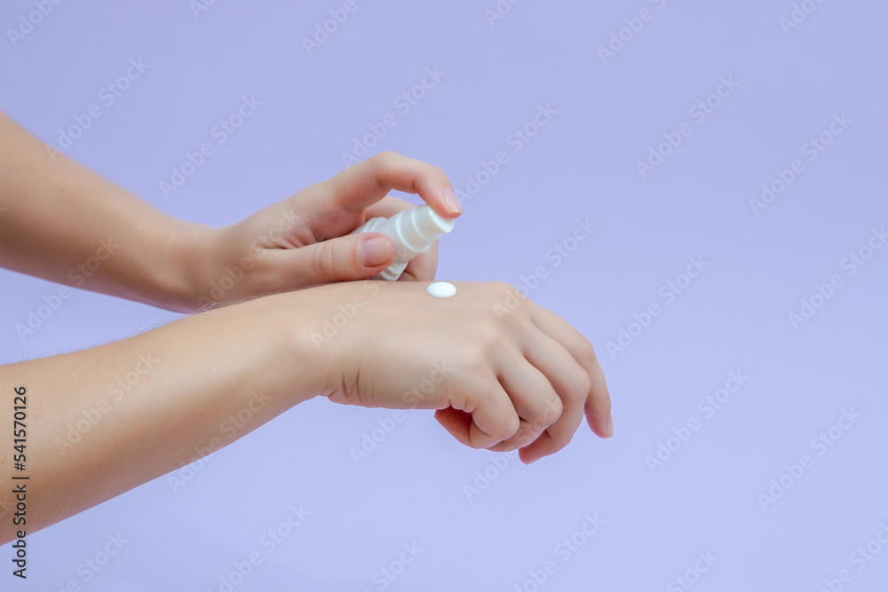 Woman's hand squeezing out cream in white tube isolated on lilac background. Beauty concept. Tube for cosmetic products