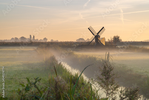 Polder landscape in the foggy morning with a small windmill.