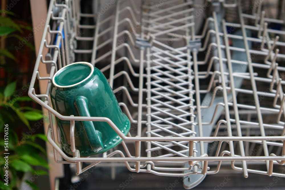 Loading the dishwasher with dirty dishes. Dirty mug. Preparing the dishwasher for the cycle of washing dirty dishes. Housework. Grey dishwasher.