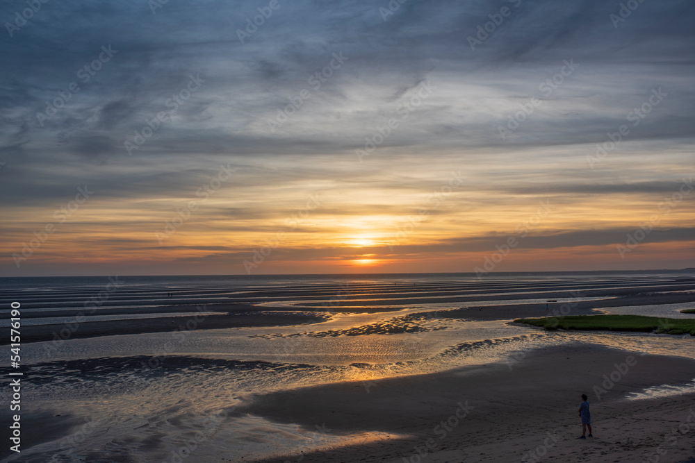 A boy looks out at the sunset during low tide A boy looks out at the sunset during low tide