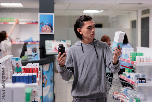 Obraz na płótnie Young adult checking medication packages, feeling indecisive about box of supplements or bottle of pills