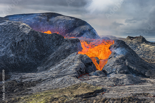 stronger lava flow from a volcanic crater. Landscape on Iceland of Reykjanes Peninsula in GeoPark. Flowing lava with more smoke and steam over the crater. dark magma around the crater