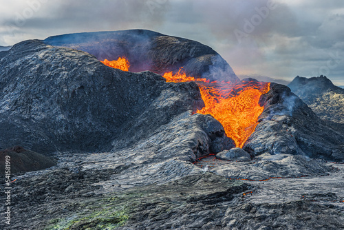 View of an active volcano. strong lava flow from crater opening. Volcanic craters on Iceland Reykjanes peninsula. Landscape in the evening with a cloudy sky. dark magma around crater opening