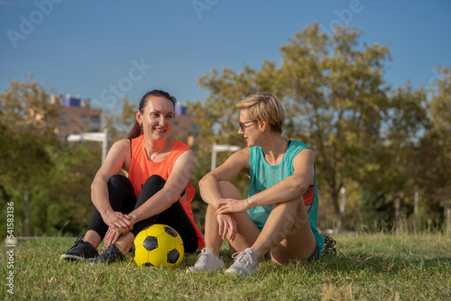 Two 30s years old woman on a training of soccer or European football in amateur team. Yellow ball, sport field with green grass.