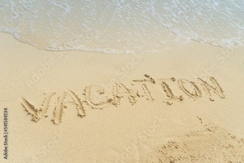 Word Vacation on beach - summer concept background. Sea, wave, sand, inscription vacation on the sand.