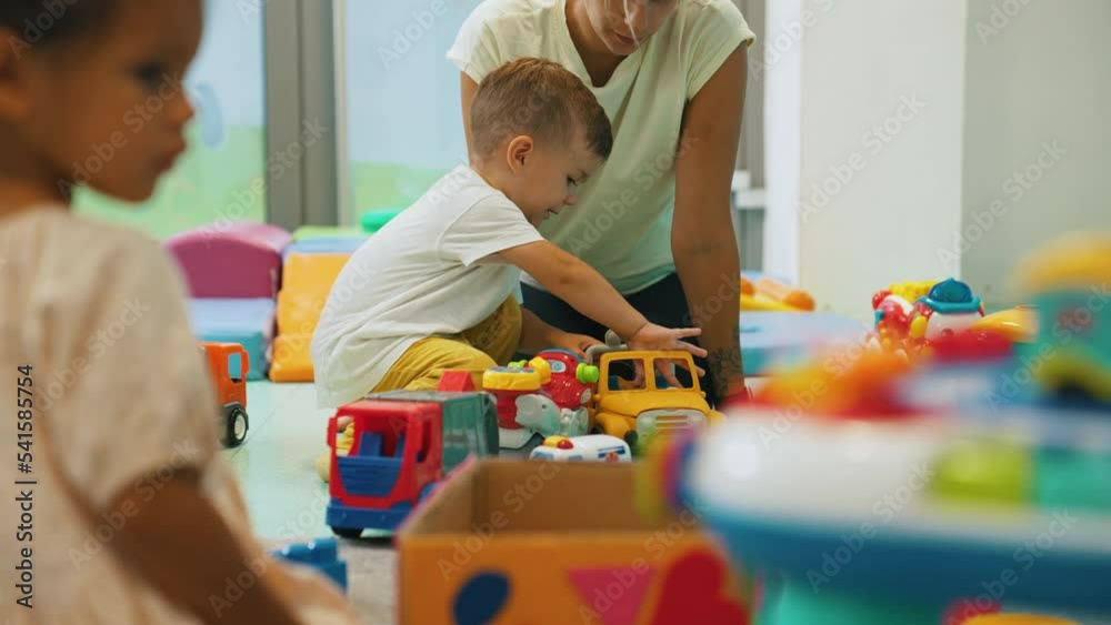 Little white boy in nursery playing with colorful toy cars with his teacher. Children during playtime. Horizontal indoor video. High quality 4k footage Little white boy in nursery playing with colorful toy cars with his teacher. Children during playtime. Horizontal indoor video. High quality 4k footage