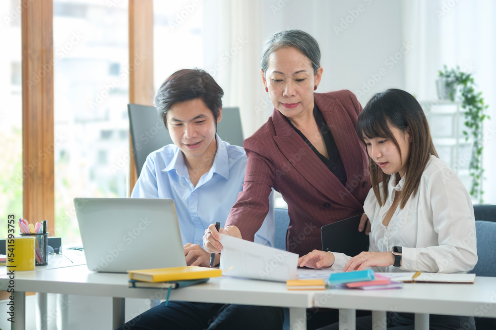 Friendly middle aged female leader having a discussion, planning new strategy with young businesspeople in office.. Friendly middle aged female leader having a discussion, planning new strategy with young businesspeople in office..