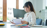 Focused asian female employee working with document and laptop at corporate office...