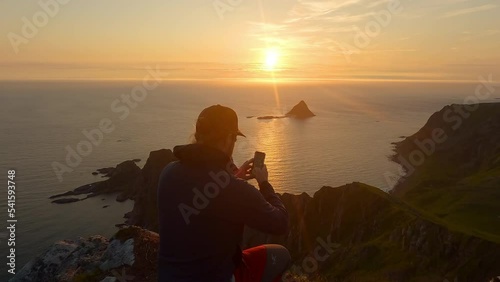 Men taking a picture with his phone of the sunset at the ocean and island Bleiksoya rock landscape in Norway photo