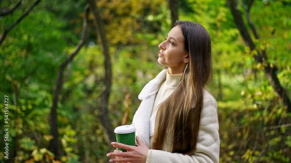 Thoughtful calm long-haired lady spending time in the autumn park. Woman enjoying the rays of sun coming through the trees. Blurred backdrop. Thoughtful calm long-haired lady spending time in the autumn park. Woman enjoying the rays of sun coming through the trees. Blurred backdrop.