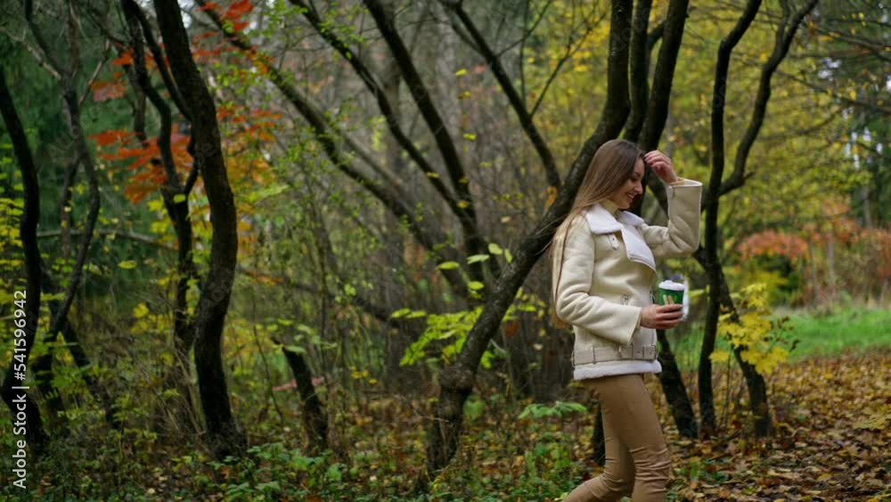 Resilient smiling mid-aged lady having a walk in the autumn park. Caucasian woman drinks coffee and enjoying warm weather. Resilient smiling mid-aged lady having a walk in the autumn park. Caucasian woman drinks coffee and enjoying warm weather.