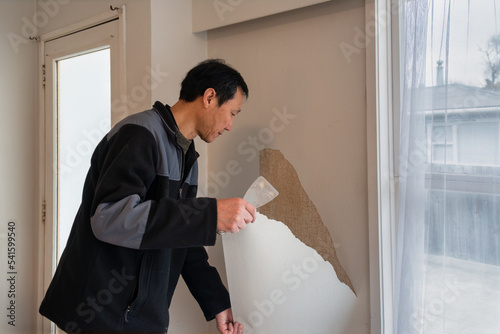 Man removing wallpaper inside an old house. Home interior do it yourself refurbishment project.
