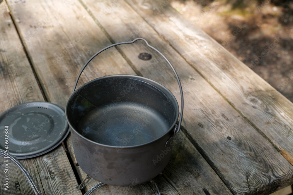A titanium pot for making food on a gas stove on a camping wooden table in the forest. High quality photo A titanium pot for making food on a gas stove on a camping wooden table in the forest. High quality photo
