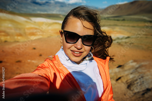 Happy young woman takes a selfie with amazing mountain view. Excited brunette enjoying vacation. Female traveller portrait.