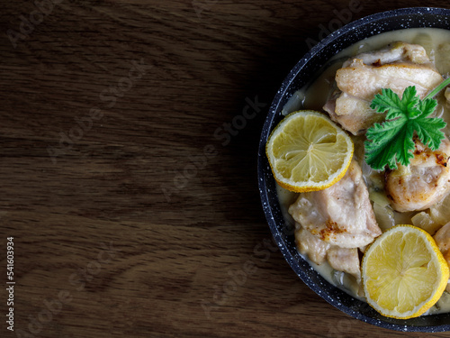 Greek stewed chicken with lemons, onions and scented leaved pelargonium leaves close-up on a iron pan on a table. horizontal, top view flat lay, copy space