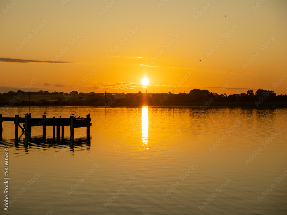 Sunrise reflecting off lake with birds gathered on pier
