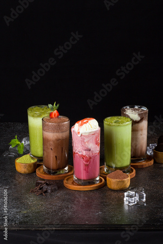 sweet milkshakes with chocolate, caramel, strawberry and whipped cream at a wooden board on table background.