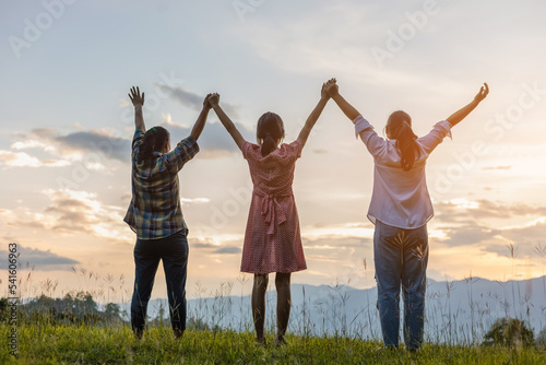 Back view of group girls friends with raising arms and enjoying sunset sky background
