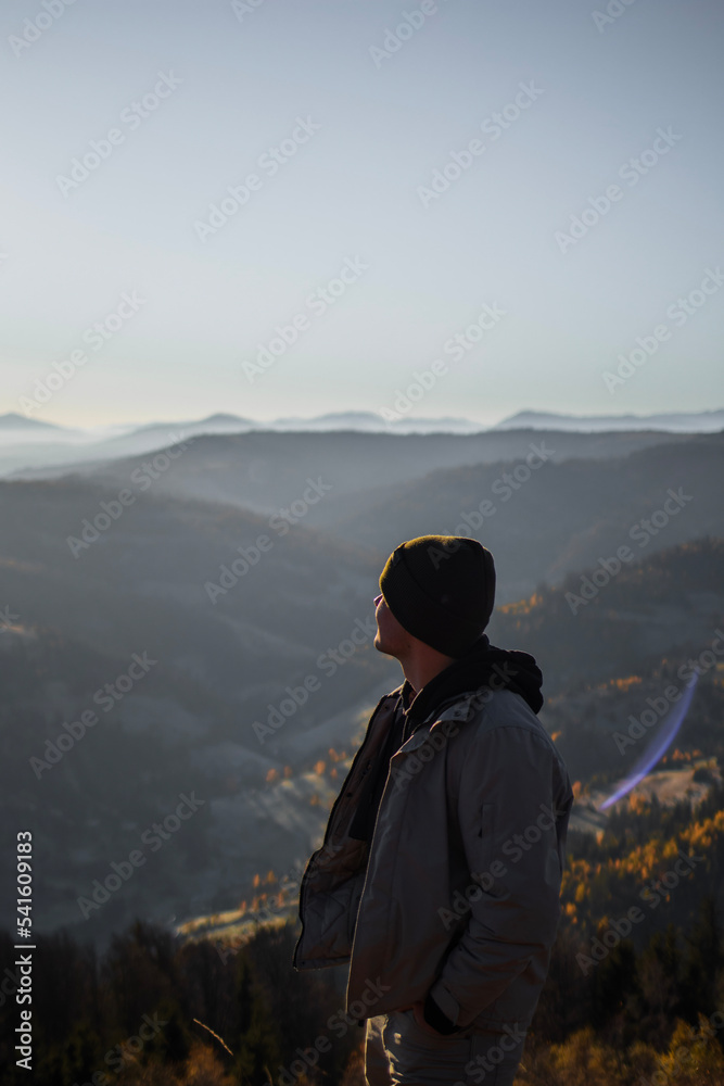 Young man is standing and looking away at the mountains autumn landscape