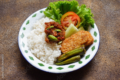 a plate of rice served with sambal and vegetables 