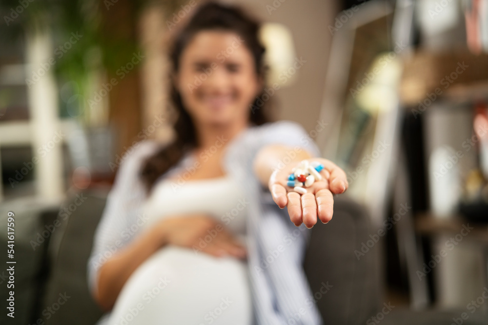 Portrait of pregnant woman holding pill. Woman taking vitamin.