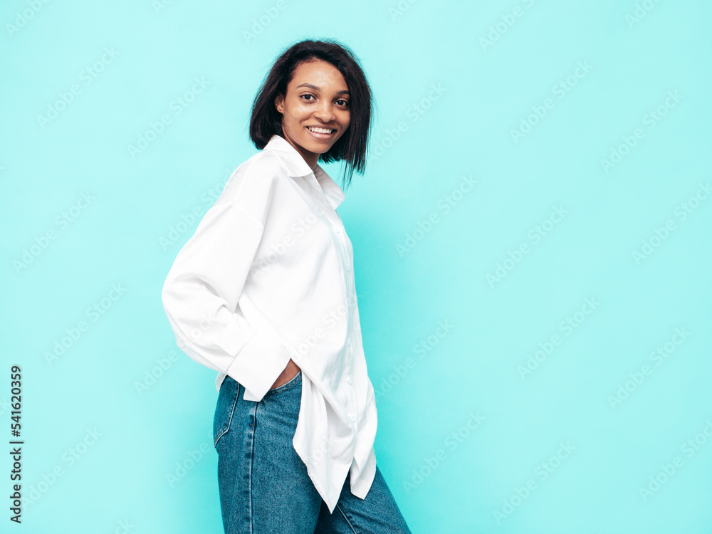 Portrait of young beautiful black woman. Smiling model dressed in summer jeans clothes. Sexy carefree female posing near blue wall in studio. Tanned and cheerful