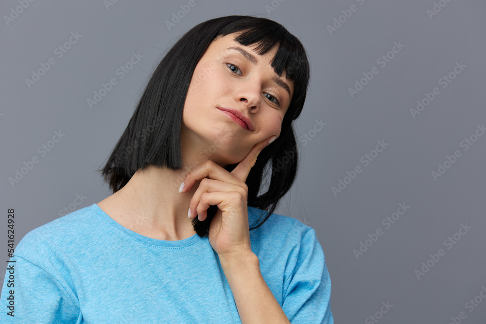 a sweet, pleasant, attractive, shy woman with black hair stands on a gray background in a blue T-shirt and looks at camera a sweet, pleasant, attractive, shy woman with black hair stands on a gray background in a blue T-shirt and looks at camera