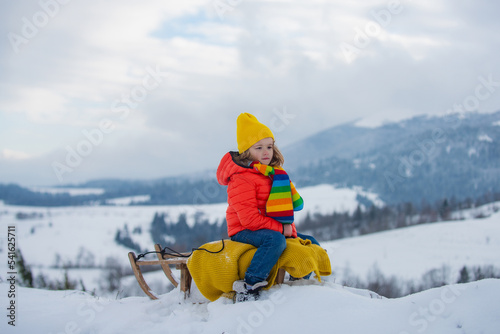 Boy sledding, enjoying sleigh ride. Child sitting on the sleigh. Children play with snow. Winter vacation concept.