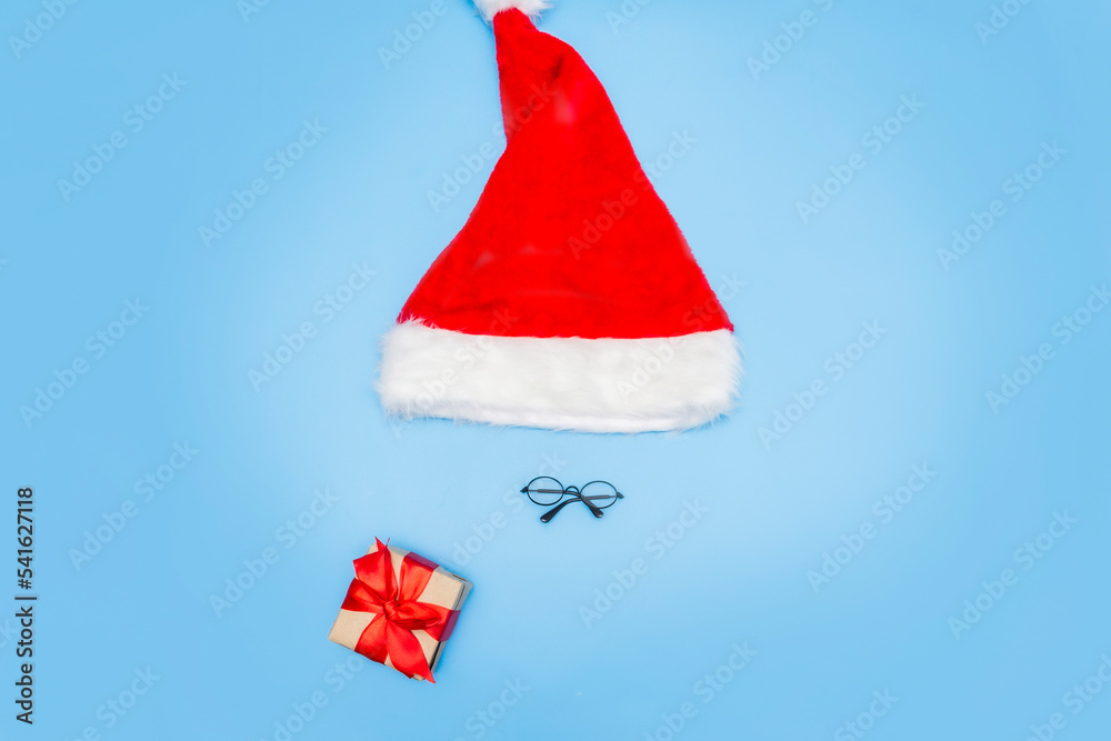 A Christmas card made of a Santa Claus hat, Santa glasses, a New Year's gift on a blue background. Top view, place for text, copy space