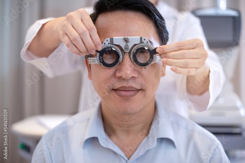 Ophthalmologist examining attractive man with optometrist trial frame, Asian male to check vision in ophthalmological clinic
