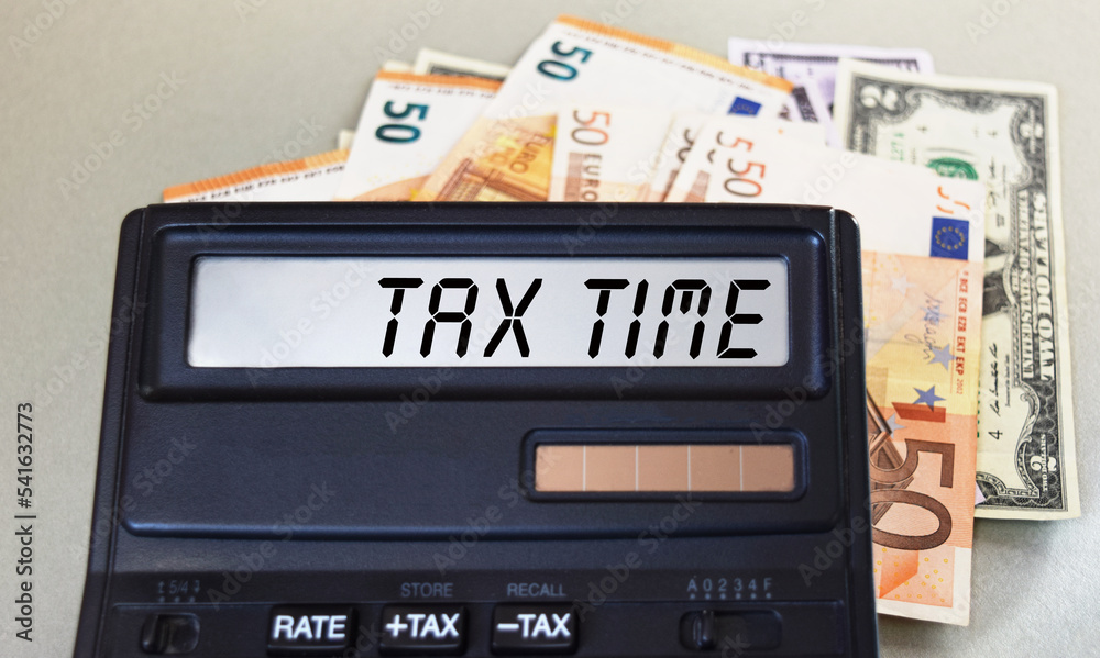 TAX TIME text written on a calculator next to the background of euro banknotes. Finance or business concept. TAX TIME text written on a calculator next to the background of euro banknotes. Finance or business concept.