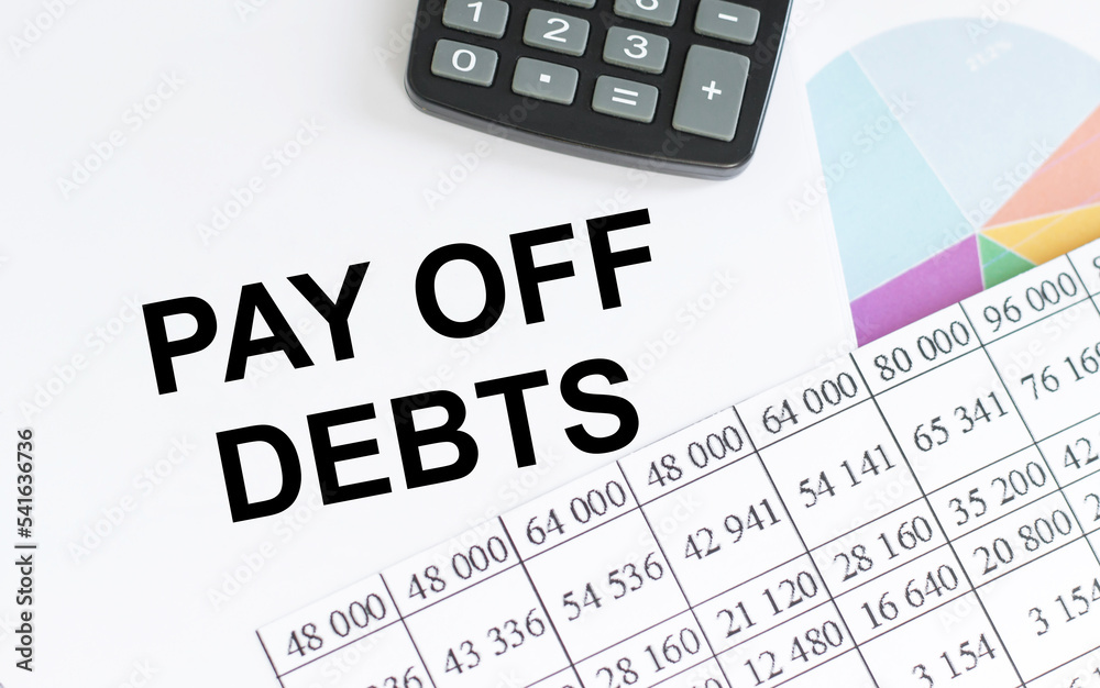 The words Pay off debts written on a white notebook. Closeup of a personal agenda. Top view. Office concept.