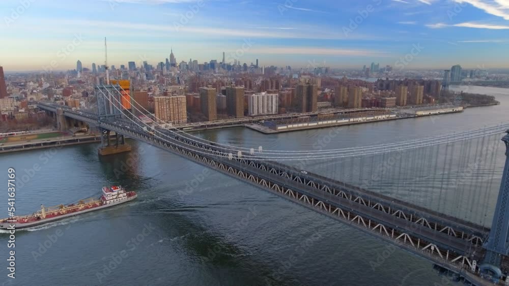Aerial Panning Shot Of Manhattan Bridge Over Ship Moving On East River By Residential City Under Sky - New York, New York Aerial Panning Shot Of Manhattan Bridge Over Ship Moving On East River By Residential City Under Sky - New York, New York