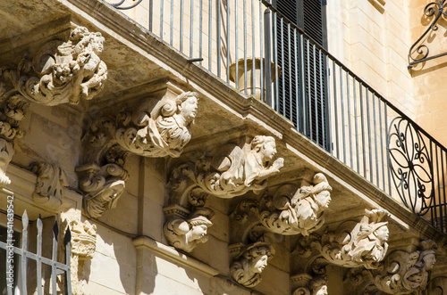 Alcune figure allegoriche scolpite in pietra leccese sorreggono il balcone della facciata di un palazzo storico di Lecce
