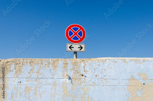 Il cartello stradale del divieto di sosta e fermata isolato in cima a un muro con dietro il cielo azzurro photo