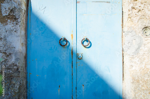 Una porta metallica azzurra con due maniglie circolari tagliata in due da una linea d'ombra in diagonale