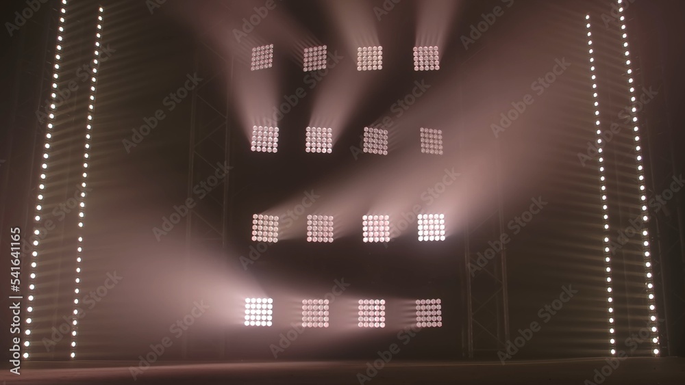 Stage light rays and smoke on empty dark concert scene. Professional lighting and light show effects on theater stage. White square spotlights and spot lights shine on black backdrop of nightclub.