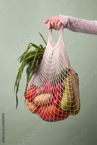 Mesh bag with vegetables and herbs in female hand.