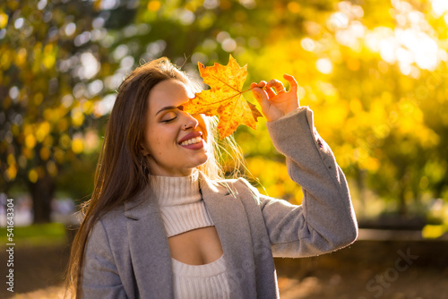 A pretty woman enjoying autumn in a park at sunset  with a leaf on her face