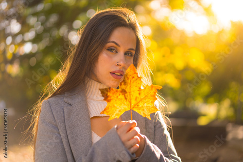 Portrait of a pretty woman enjoying autumn in a park at sunset  with a leaf from the tree