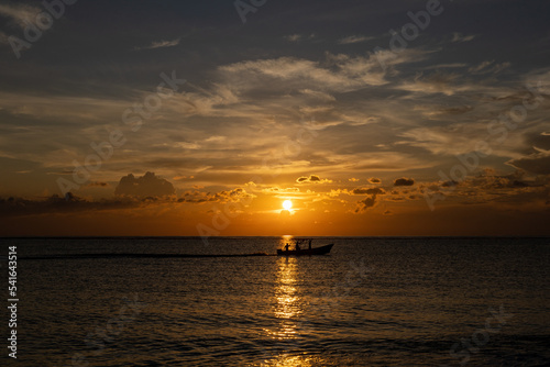 Scenic sunset in the Playa de la Cueva Beach  Cabo Rojo  Pedernales  Dominican Republic. Vibrant colors  sun above water falling in the sea  with boat silhouette passing by.