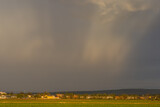 flat landscape with houses and sunrays between rainclouds