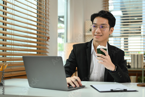 Handsome male investor drinking coffee and analyzing financial data on laptop computer