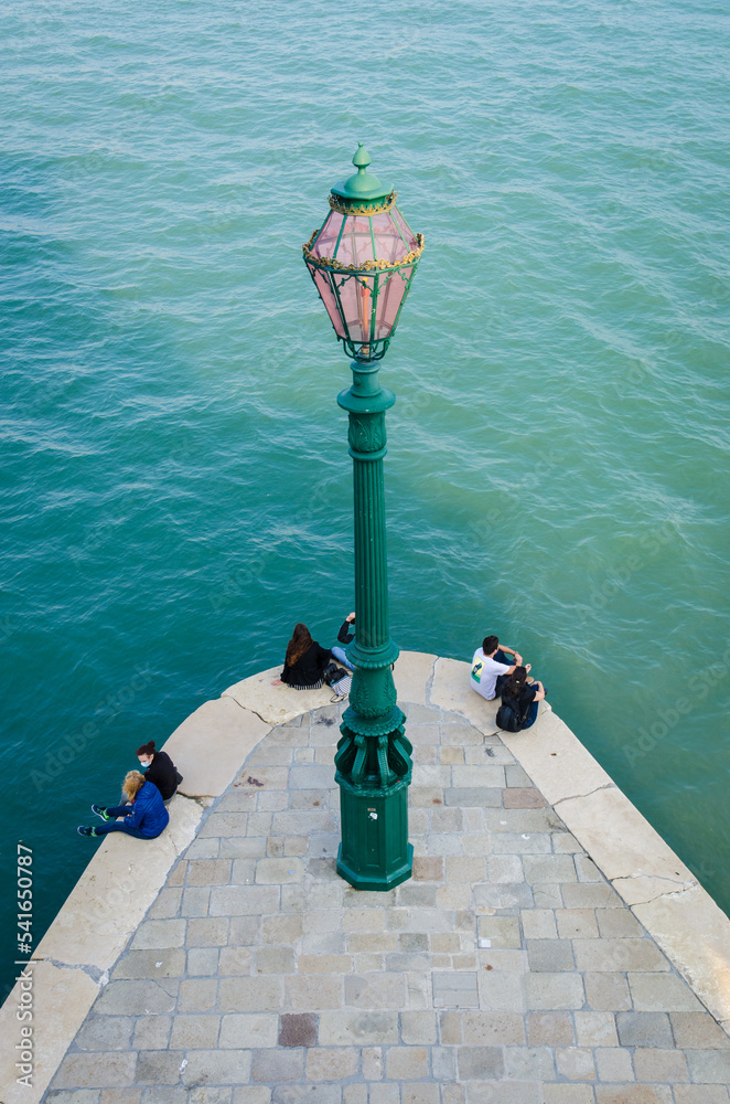 Il lampione della punta della dogana a Venezia visto dall'alto con delle persone sedute sulla riva a parlare Il lampione della punta della dogana a Venezia visto dall'alto con delle persone sedute sulla riva a parlare