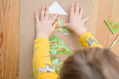 Making a Christmas tree. Boy gluing stamped colorful triangles in to the spruce shape tower. Preschool or nursery type activities at home. Montessori task for hand coordination, fosterage imagination