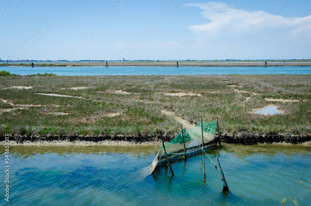 Caratteristico paesaggio della laguna nord di Venezia verso Lio Piccolo con delle reti da pesca in una giornata primaverile di sole