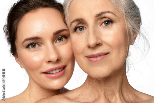 Two generations of beautiful women, mother and daughter, hugging sweetly and looking. Close-up portrait about caring for different facial skin types and good intergenerational relationships.