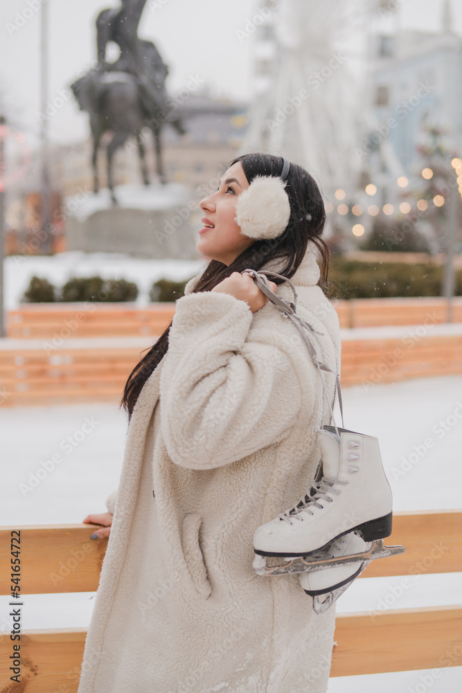 Obraz premium Beautiful caucasian woman in warm cozy clothes skating on ice rink as snow falls. Cold happy winter day in festive city. Holidays, Christmas, New Year, beauty concept.