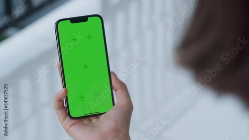 Point of View of woman holds one hand mobile phone and watching a video on the background of a floor with white tiles. Use green screen for copy space closeup. Chroma key mock-up on smartphone. 