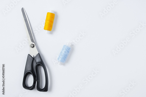 Fabric scissors and sewing thread. White background. View from above.